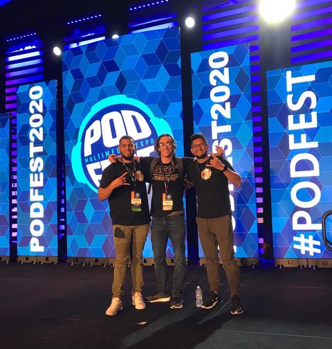 Matt Bertram with two other attendees on the Podfest Multimedia Expo stage, the Podfest logo on the screens behind them