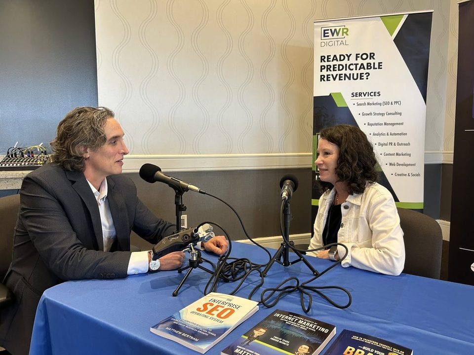 Matthew Bertram interviewing a guest at a table with microphones, his books on the table